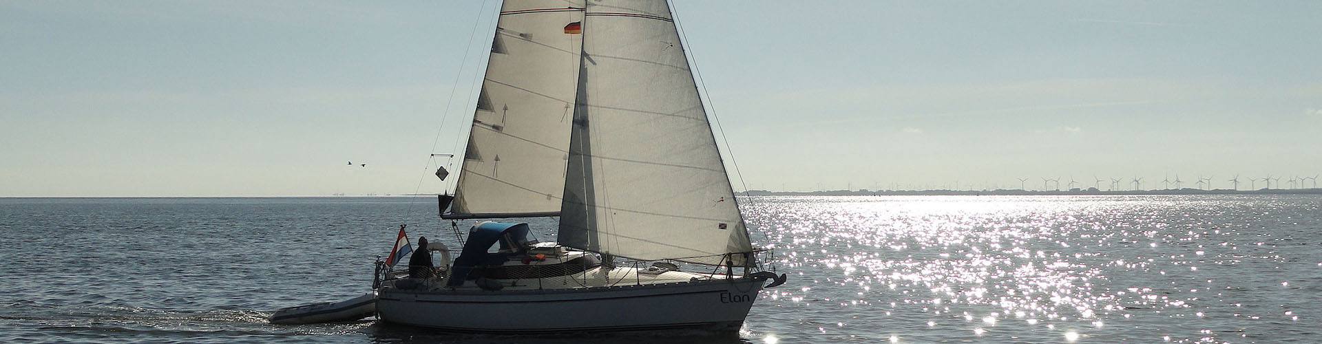De Elan in tegenlicht op glinsterend water, met windmolens aan de horizon