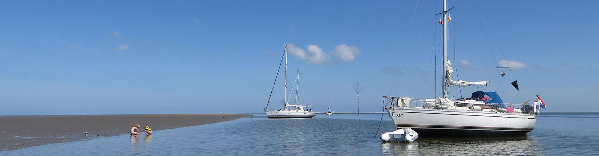 Twee kinderen spelen in het ondiepe water bij een zandplaat, met de Elan en een andere zeilboot voor anker